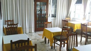 A dining area with tables and chairs, a wooden door, and a window with curtains. - Pensão Residencial Vila Teresinha (Funchal)