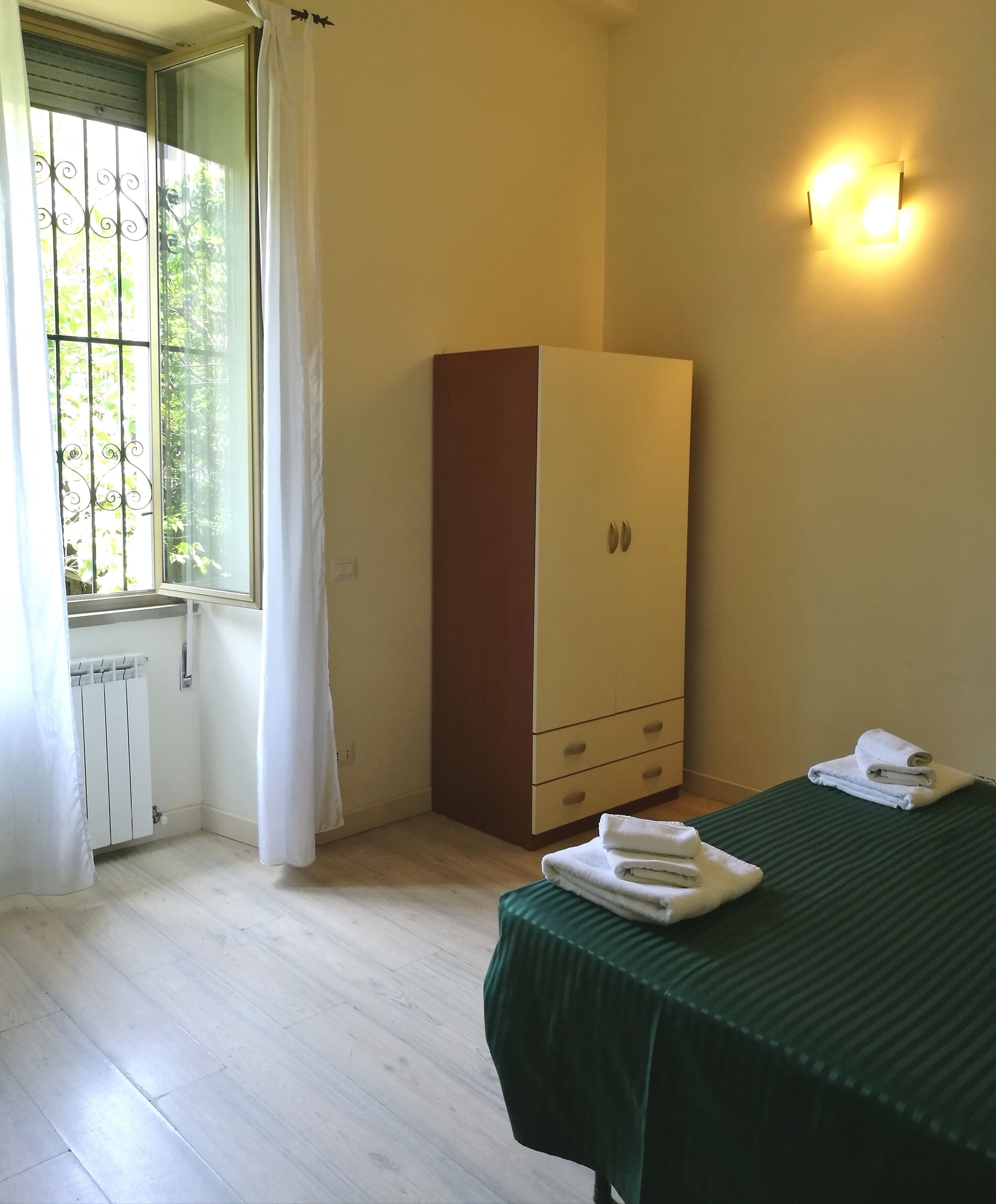 Une chambre avec un lit, une armoire, un radiateur et une fenêtre avec des rideaux.