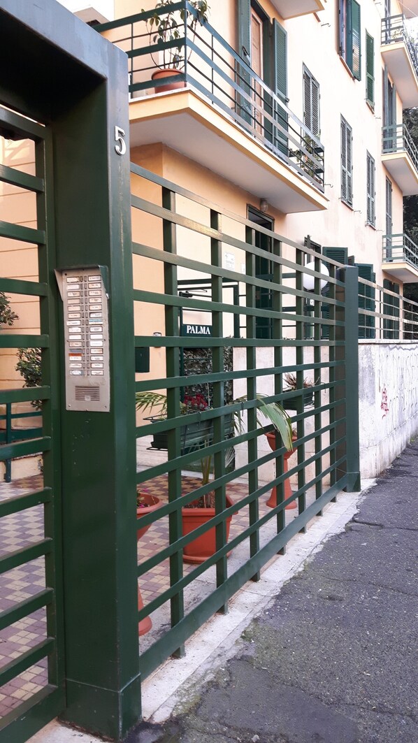 A gated entrance with a metal gate, a sign reading "PALMA", and a building with balconies and windows in the background. - Palma Residence (Rome)
