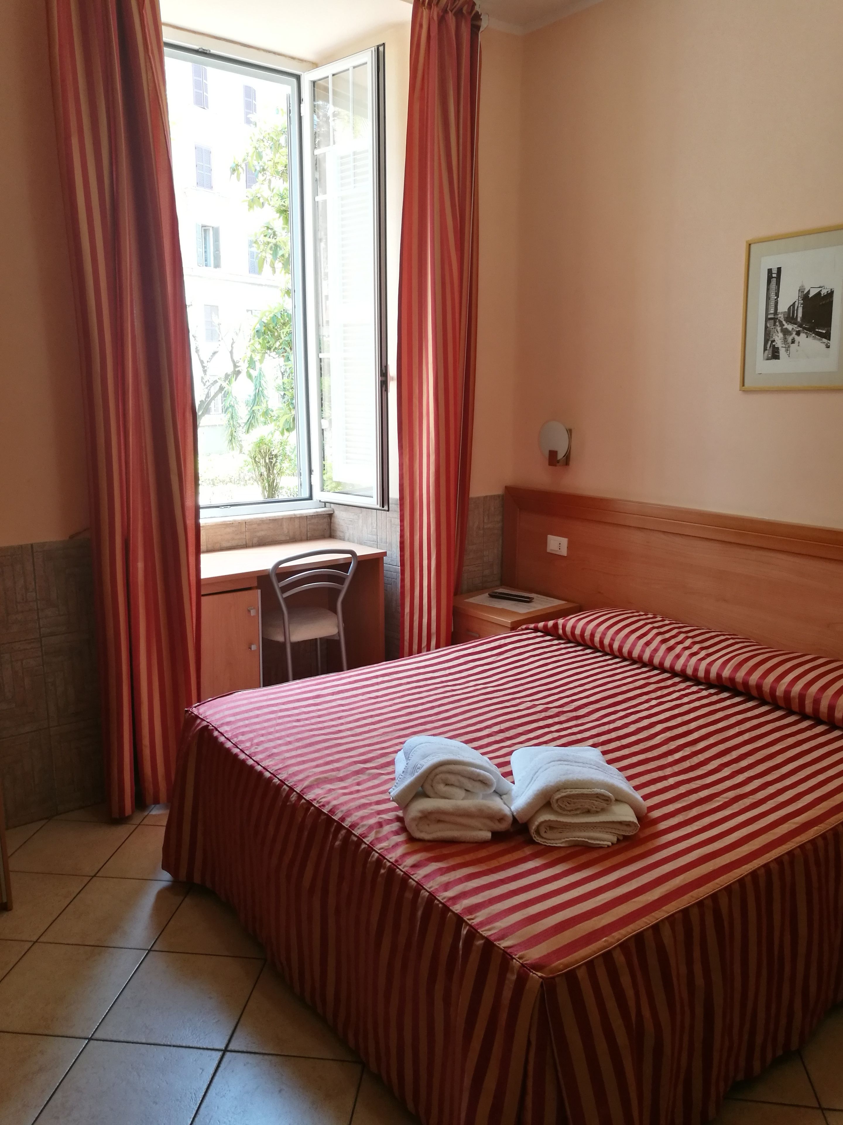 Una camera d'albergo con un letto, una scrivania e una finestra con tende.
