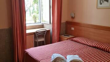Una camera d'albergo con un letto, una scrivania e una finestra con tende.