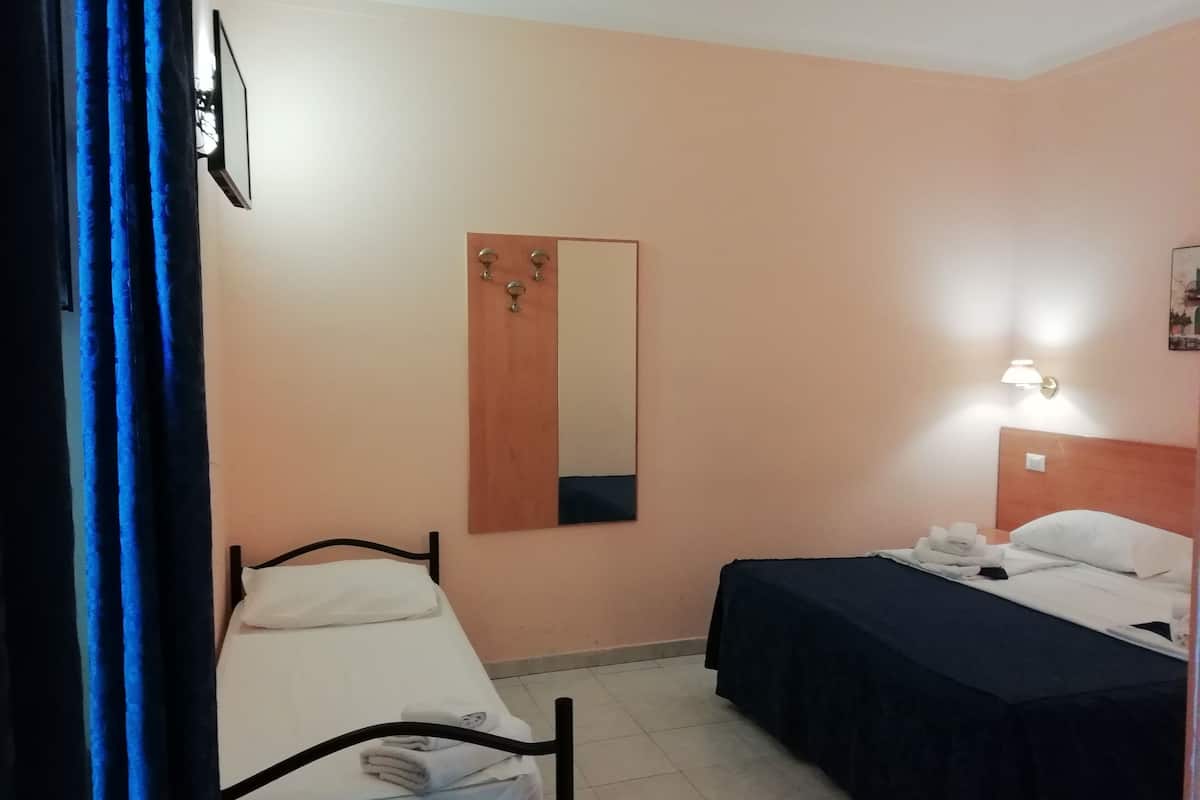 Pieni hotellihuone, jossa on kaksi erillistä sänkyä, puuovi, seinälle kiinnitetty peili ja yöpöytälamppu.