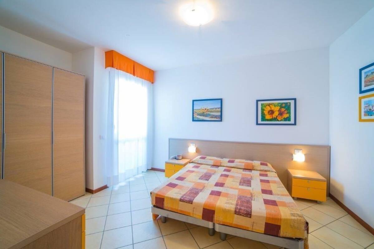 A bedroom with a bed, two bedside tables, a wardrobe, and a window with curtains.