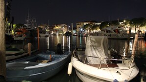 A marina at night with boats docked, calm water, and buildings in the background.