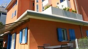 A multi-story residential building with balconies, a flat roof, and a small outdoor seating area.