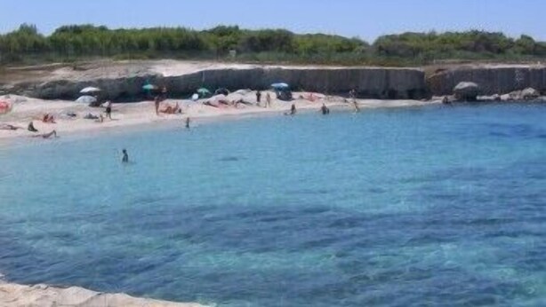 A beach with clear blue water, people swimming and sunbathing, and a rocky shoreline. - Resort Puntacassano (Melendugno)