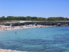 A beach with clear blue water, people swimming and sunbathing, and a rocky shoreline. - Resort Puntacassano (Melendugno)