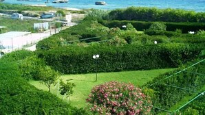 A landscaped garden with a view of the sea, featuring neatly trimmed hedges and a small flower bed. - Resort Puntacassano (Melendugno)