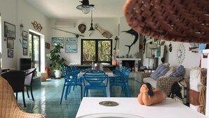A spacious living room with a dining area, large windows, and various wall decorations. - Resort Puntacassano (Melendugno)