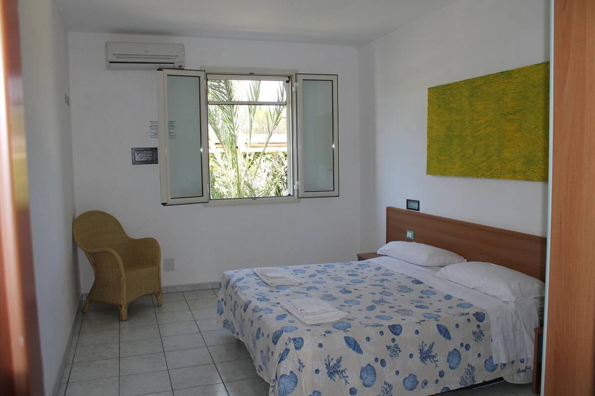 Une chambre avec un lit, une chaise, une fenêtre et un climatiseur fixé au mur.