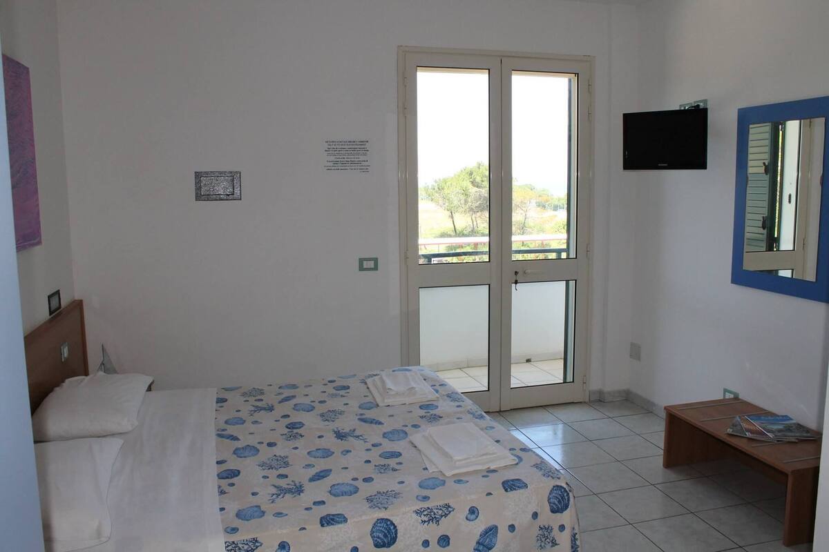 Une chambre avec un lit, une petite table, un téléviseur et une porte-fenêtre coulissante donnant sur un espace extérieur.