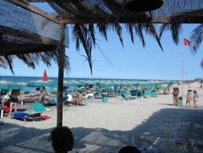 A beach with umbrellas and lounge chairs, a clear sky, and a flag on a pole.