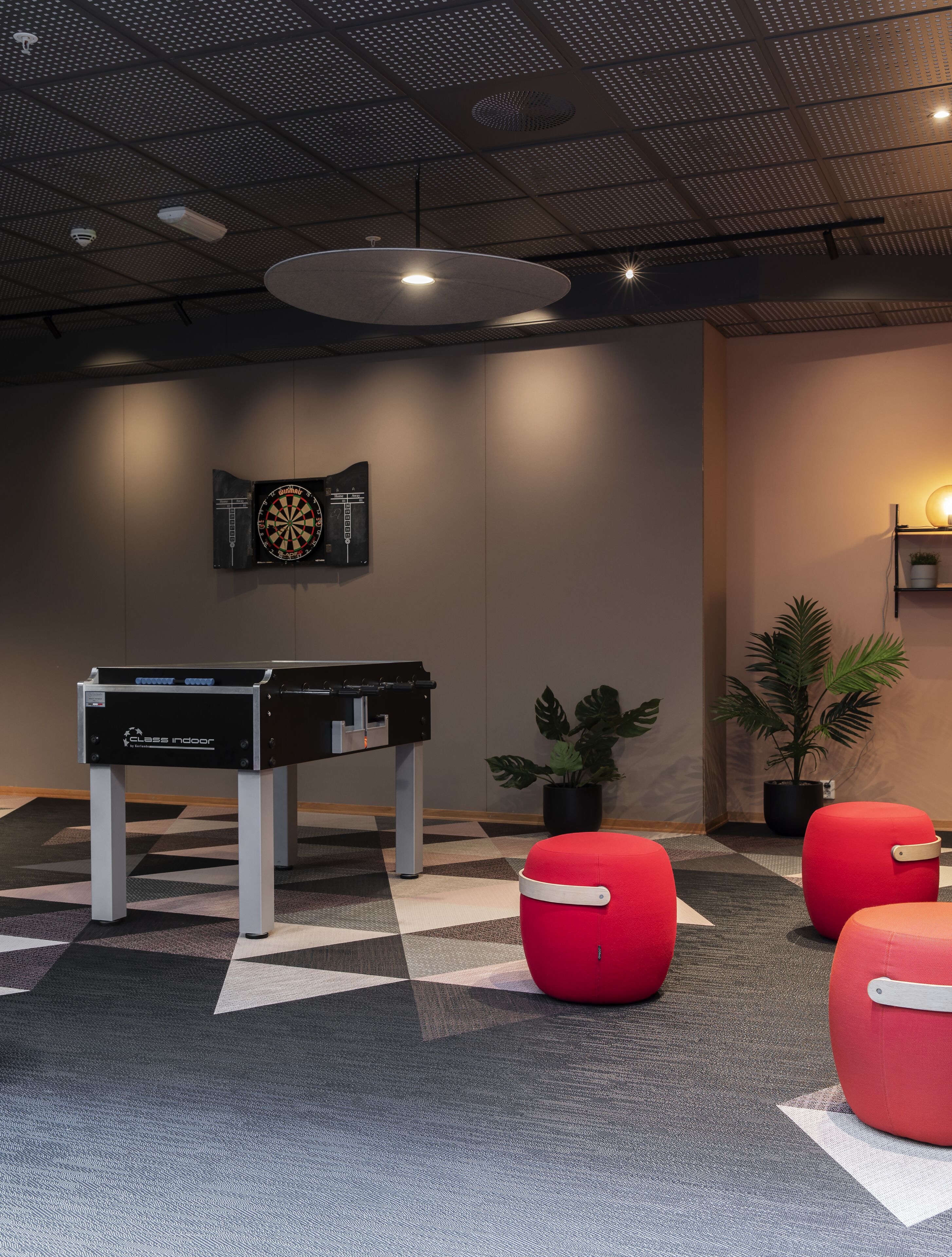A modern indoor space with a foosball table, red seating, and potted plants.