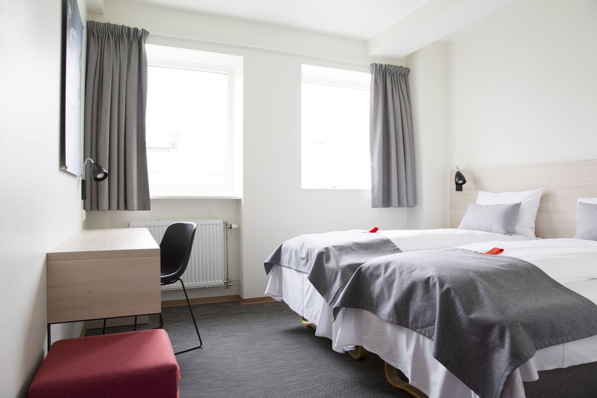 Hotellihuone, jossa on kaksi sänkyä, työpöytä, tuoli ja patteri.