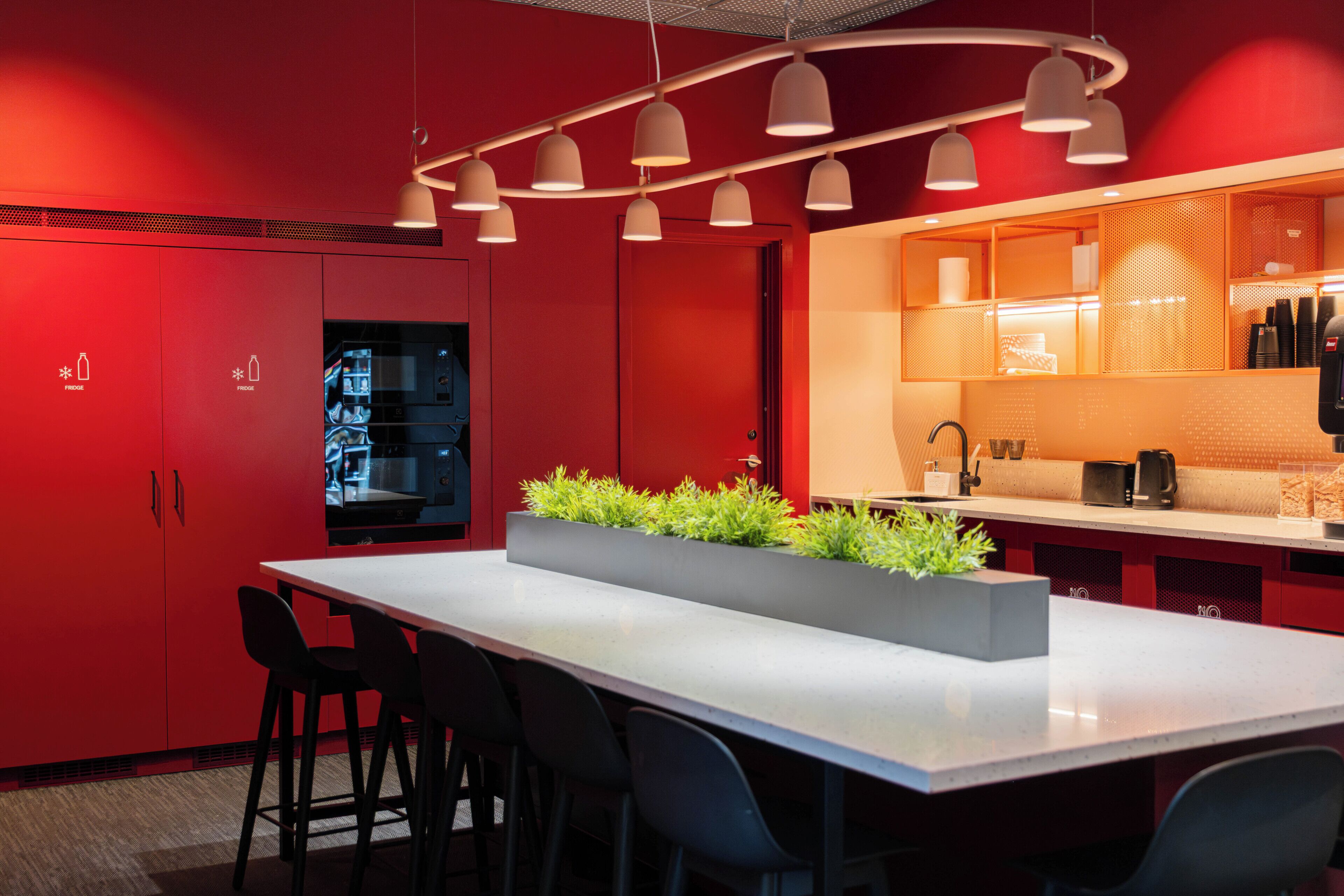 Una cocina moderna con armarios rojos, una isla central con plantas e iluminación colgante.
