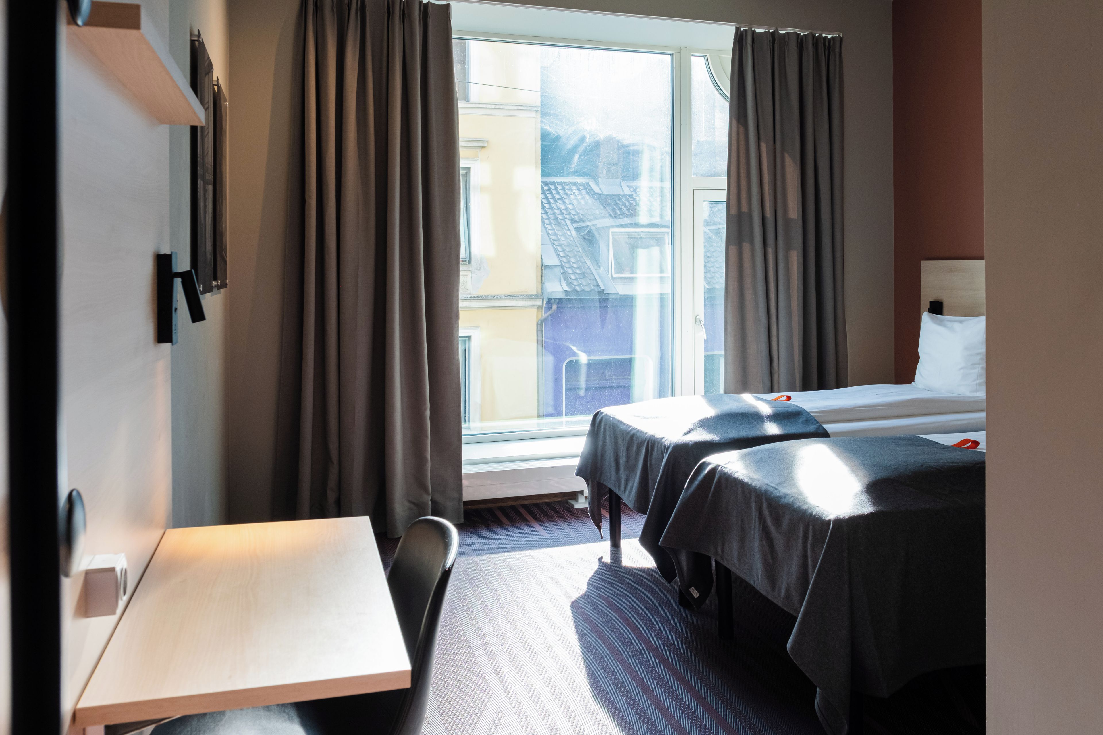 A hotel room with two beds, a desk, and a window with curtains.