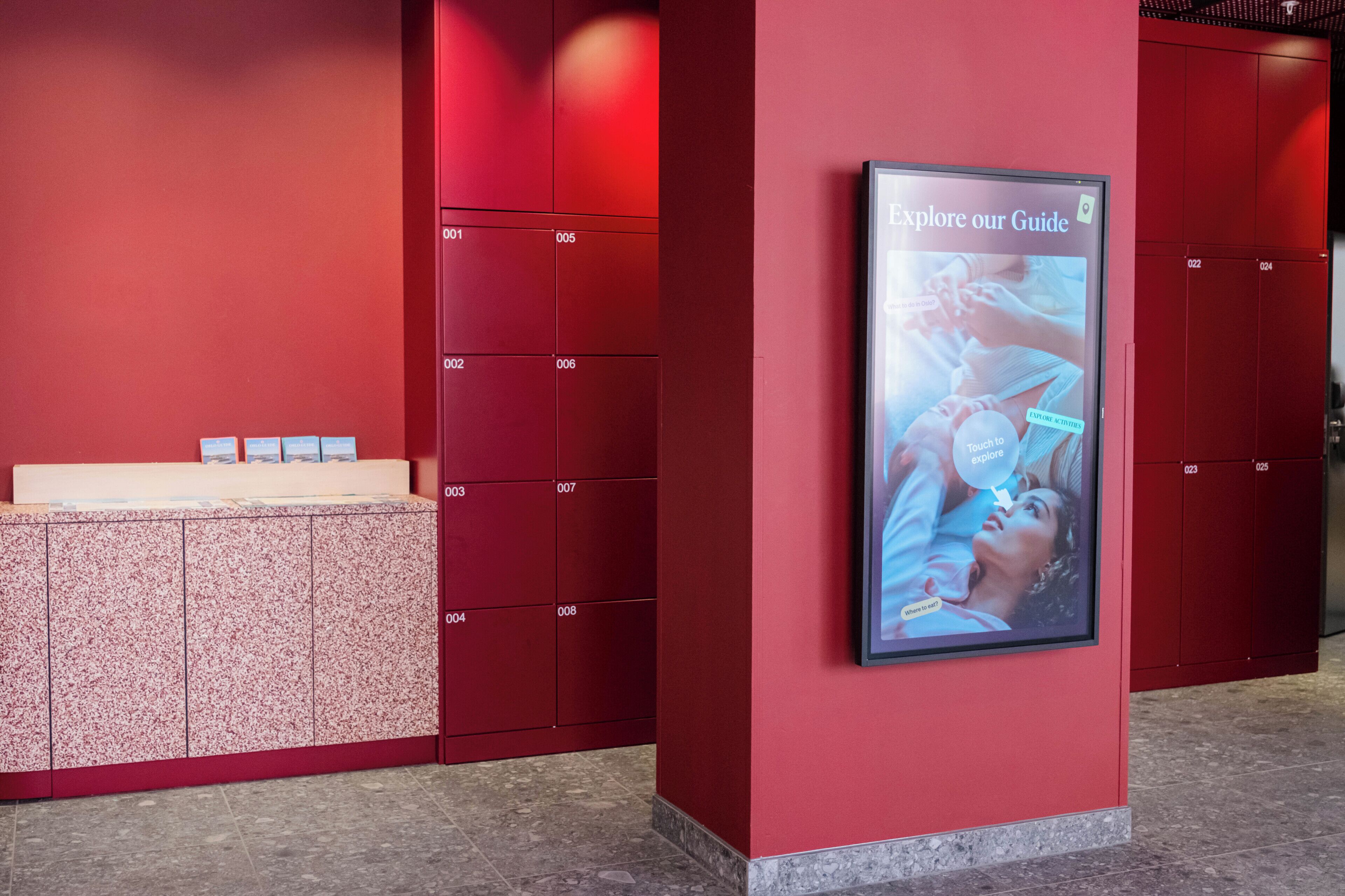 A red wall with lockers and a digital screen displaying a guide.