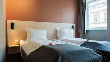 A hotel room with two beds, a nightstand, a wall-mounted light, and a window with curtains.
