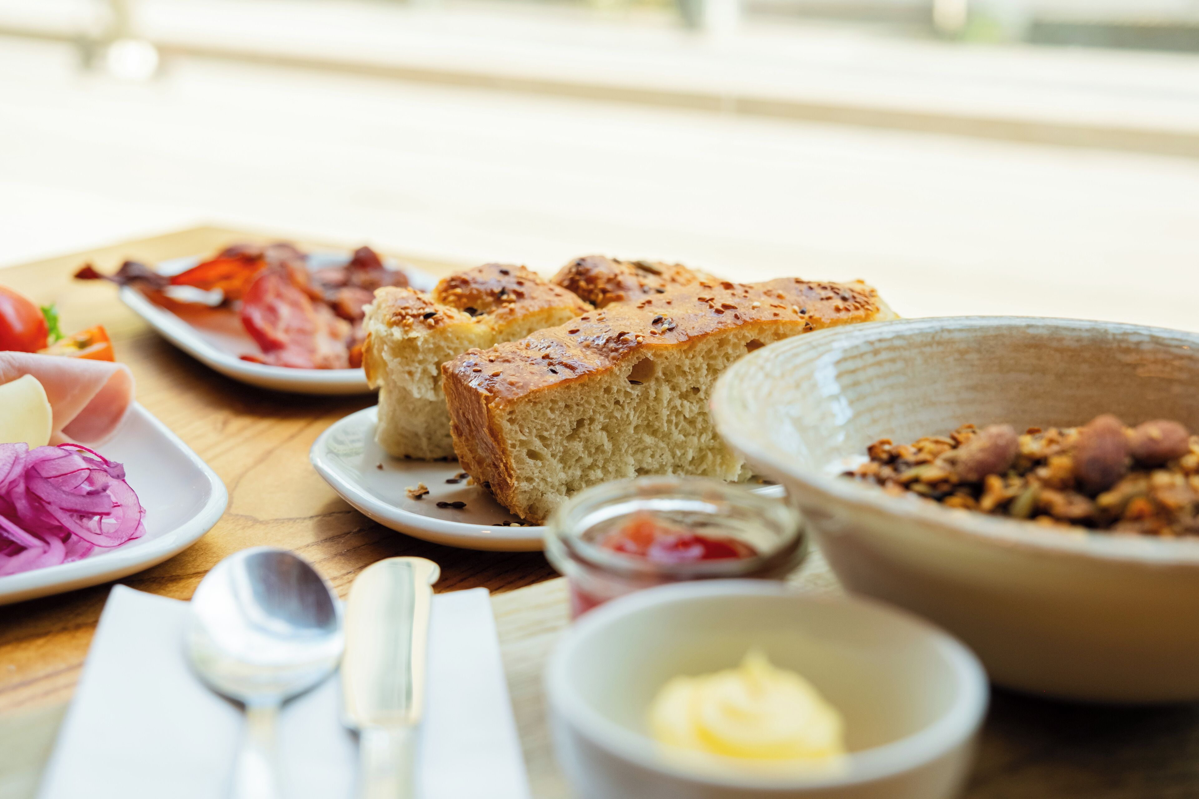 Impostazione per la colazione con pane, uova e diversi condimenti su un tavolo di legno.