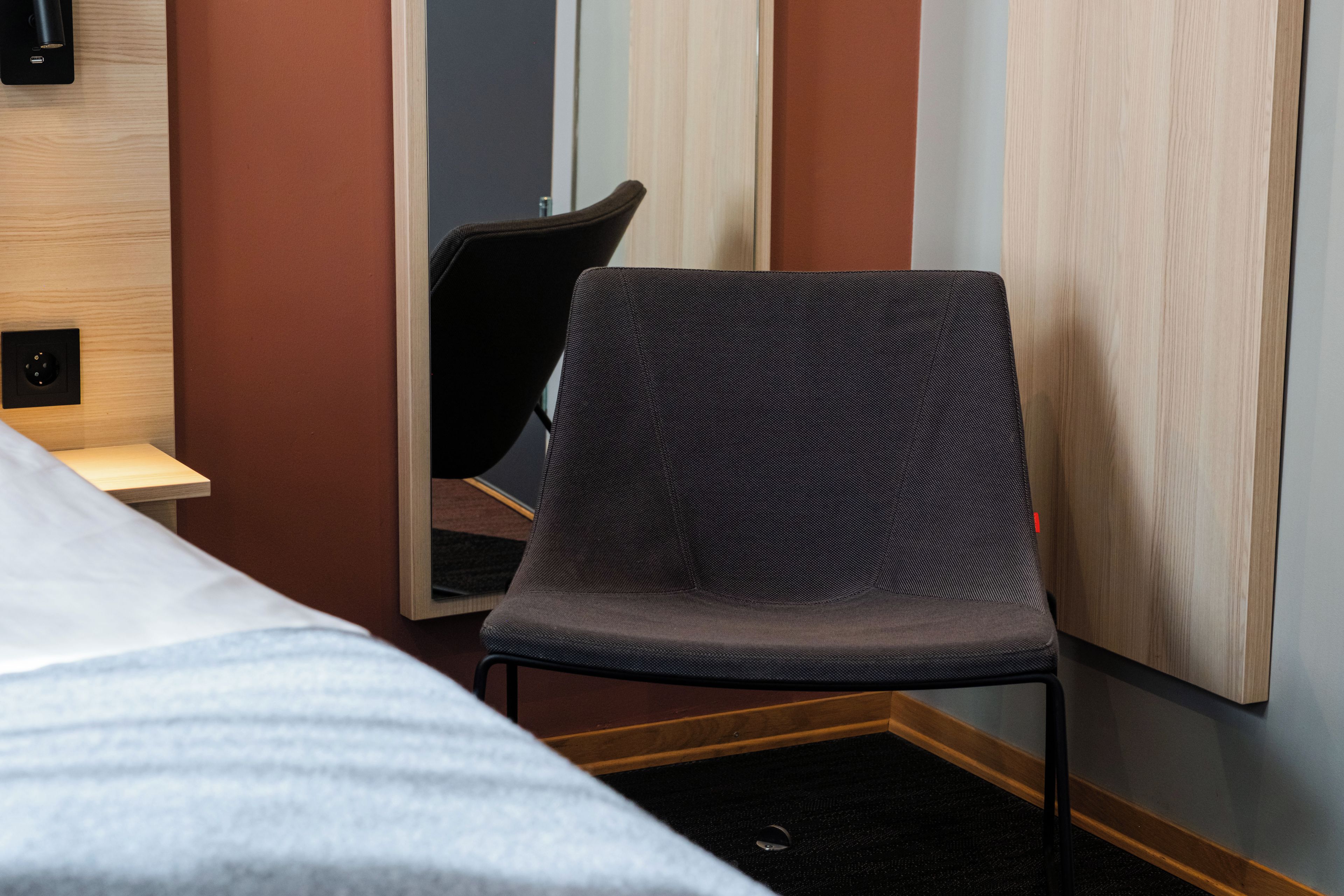 A hotel room with a bed, a chair, a desk, and a mirror.