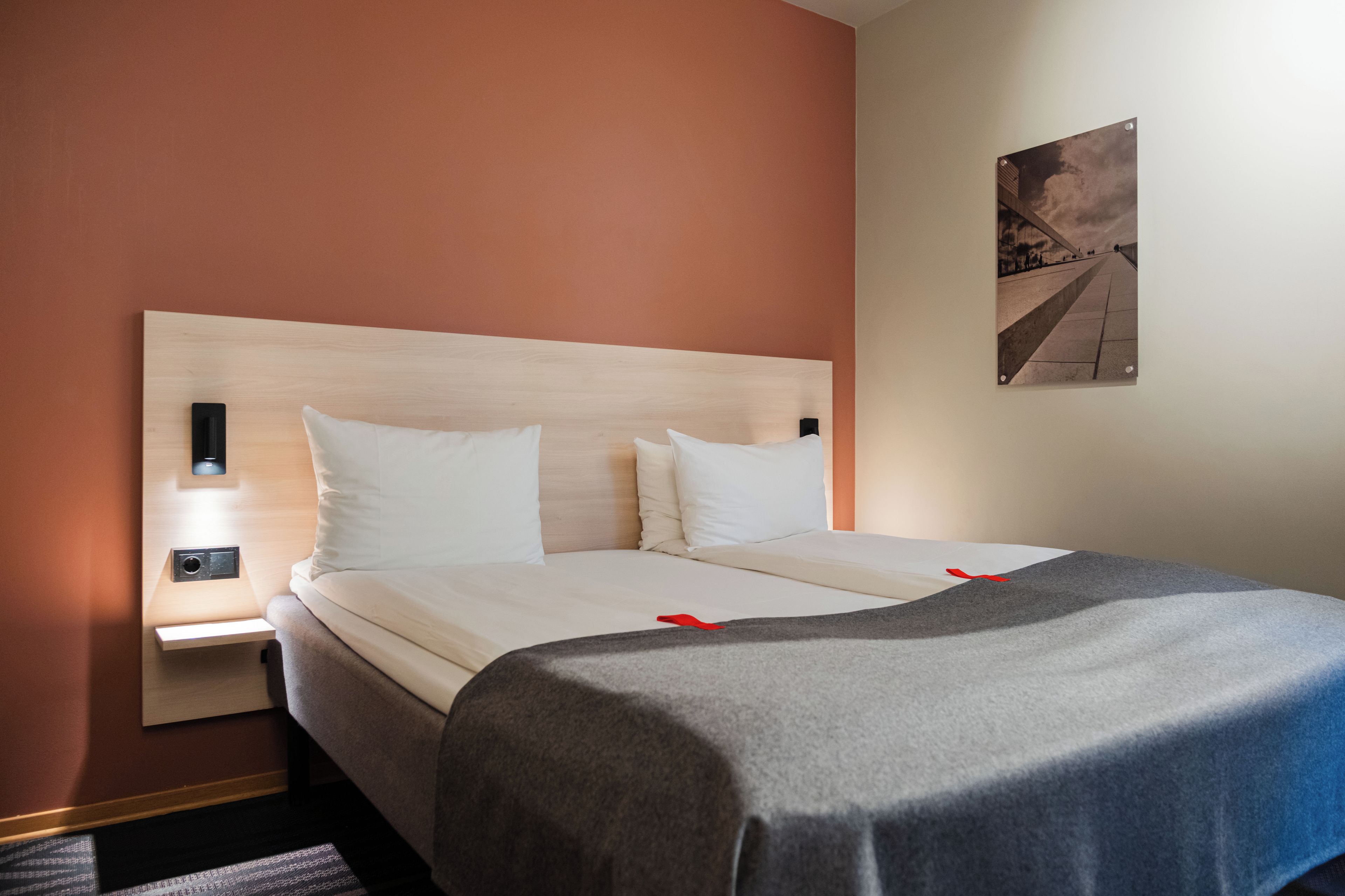 A hotel room with a bed, a nightstand, a lamp, and a painting on the wall.