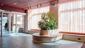 A lobby with a large potted plant, a seating area with orange cushions, and a glass door entrance. - Citybox Oslo (Oslo)