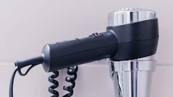 A hair dryer with a coiled cord plugged into a wall socket.