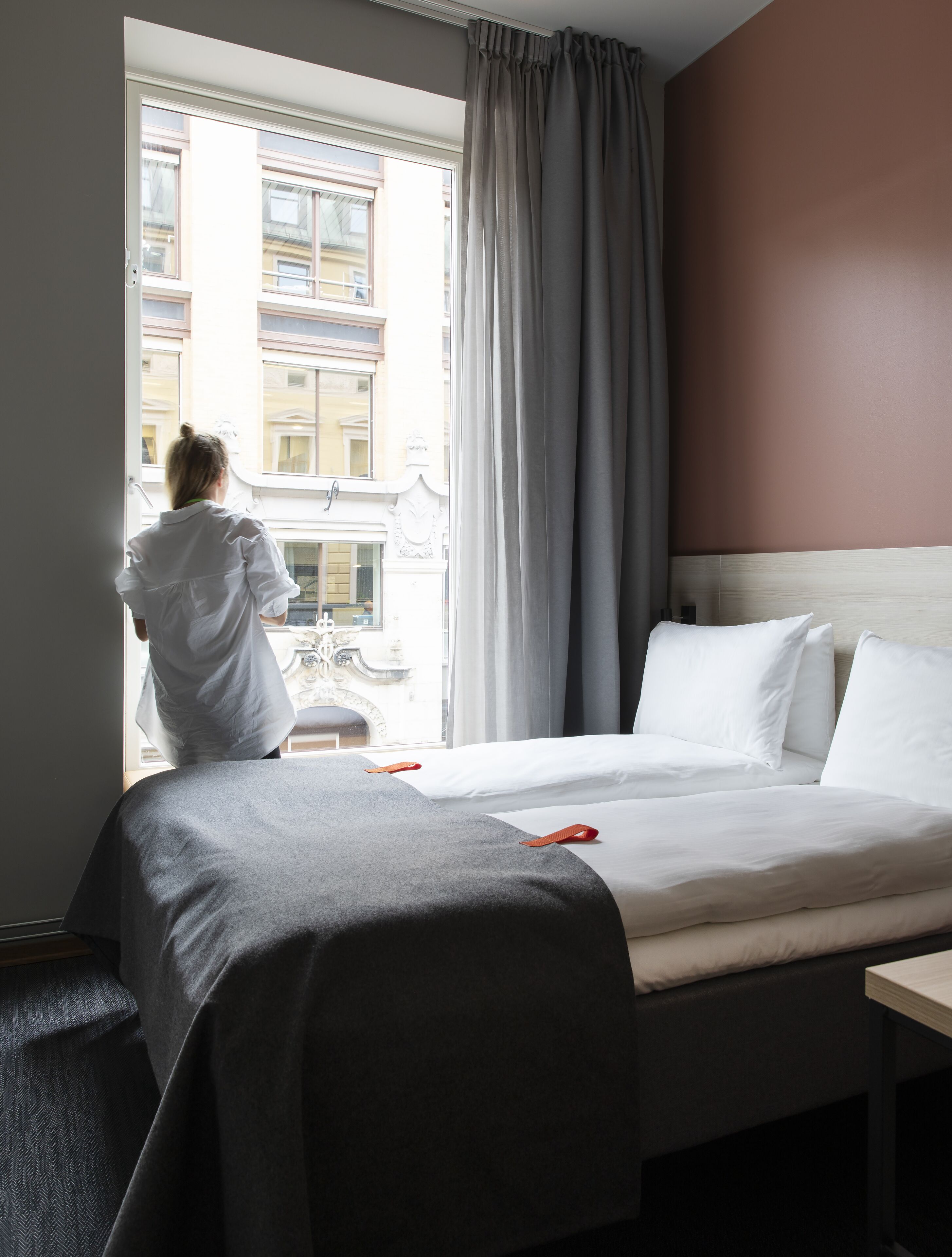 Une chambre d’hôtel avec un grand lit, une fenêtre avec des rideaux et une vue sur les bâtiments environnants.