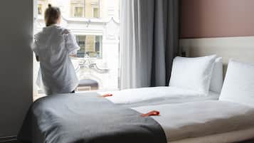 Een hotelkamer met een groot bed, een raam met gordijnen en uitzicht op gebouwen.