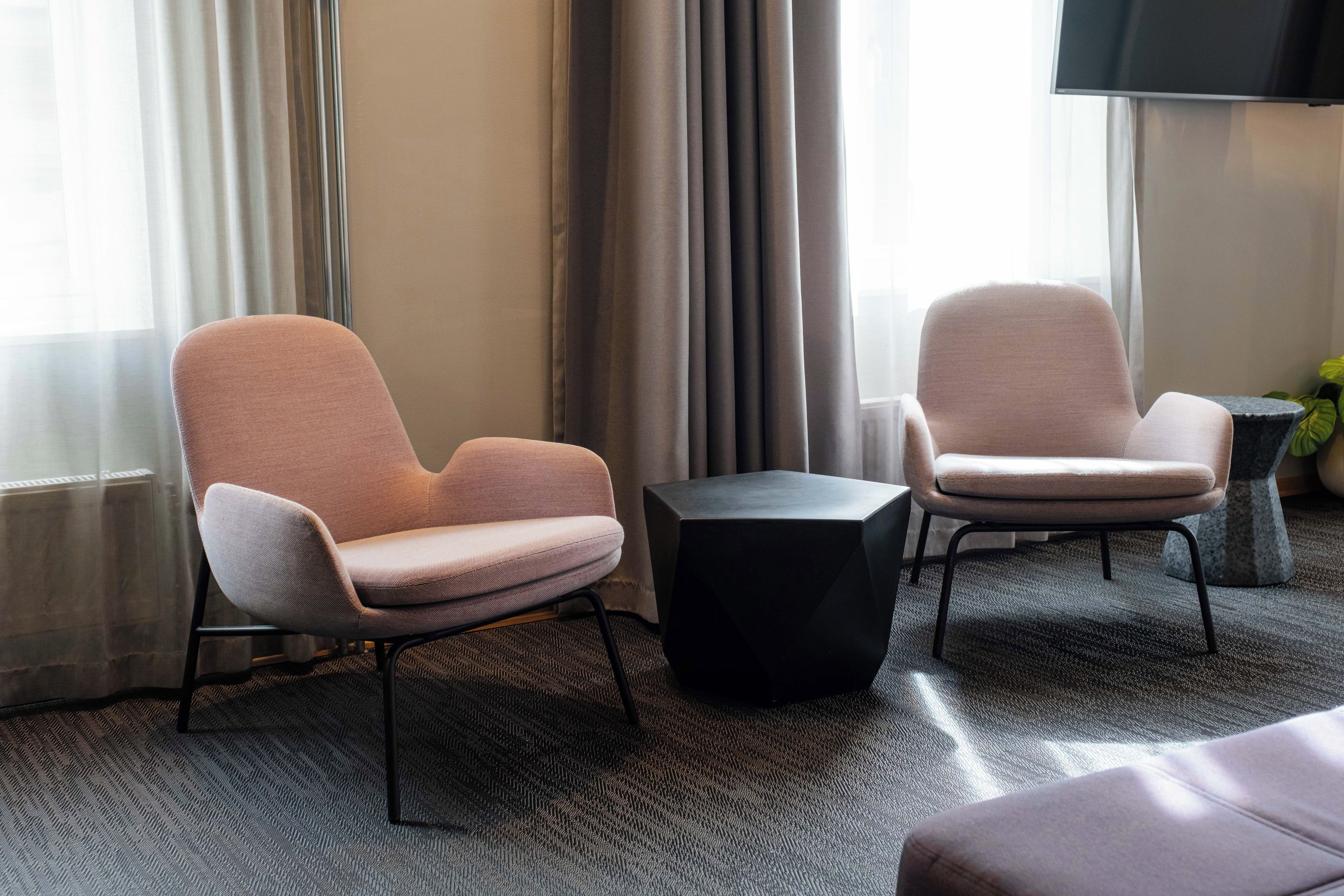 A modern hotel room with two armchairs, a small black table, and a large window with curtains.