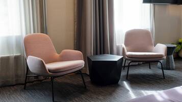 A modern hotel room with two armchairs, a small black table, and a large window with curtains.
