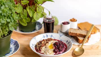 A breakfast setting with a bowl of oatmeal topped with nuts and berries, a glass of juice, and slices of toast on a wooden table.