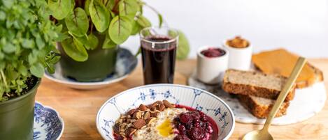 Une table en bois dressée pour le petit-déjeuner, avec un bol de porridge garni de noix et de fruits rouges, un verre de jus et des tranches de pain grillé.