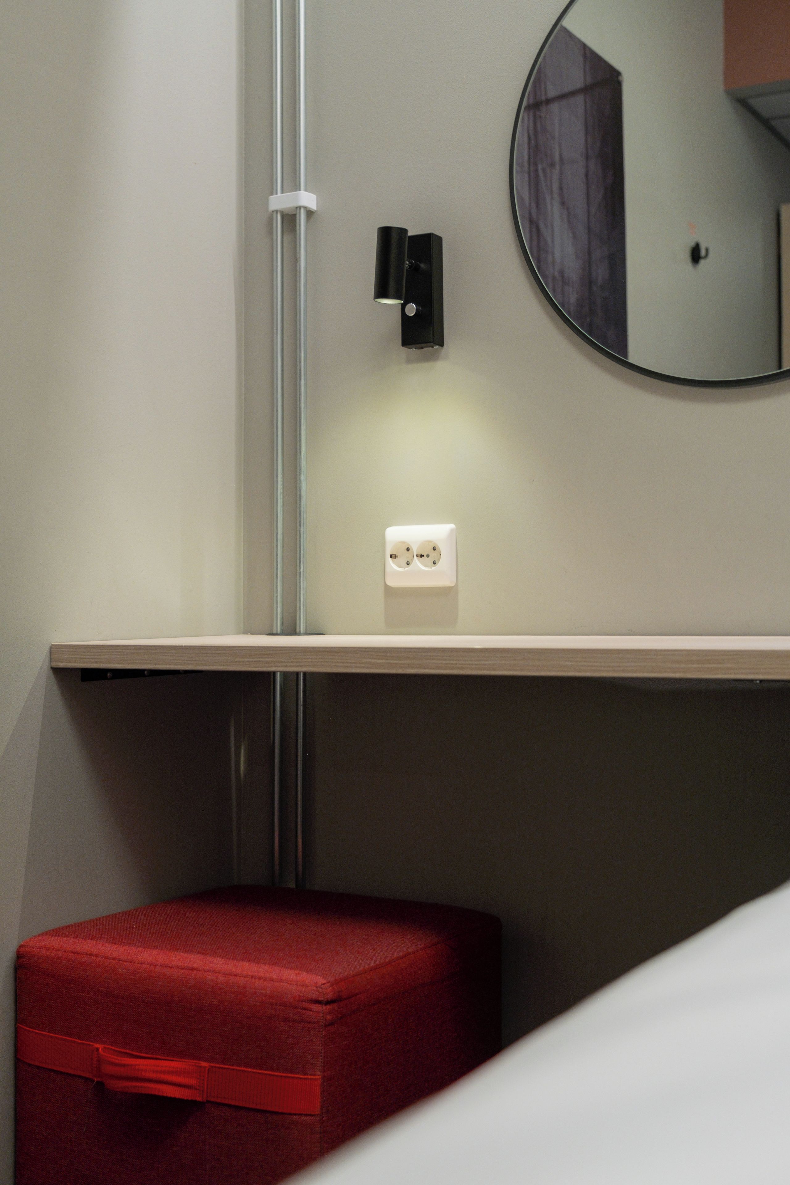 A small, enclosed space with a red storage unit, a wall-mounted light, and a round mirror reflecting part of the room.