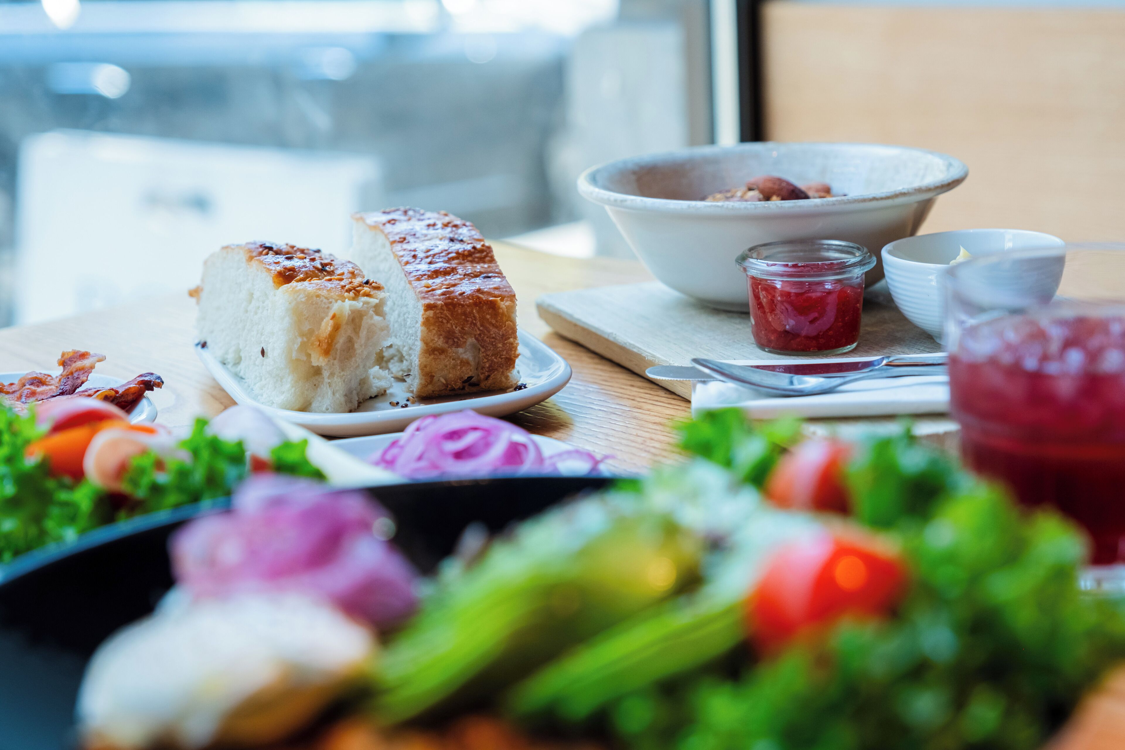 A table with a plate of bread, a bowl of berries, a glass of red drink, and a salad.