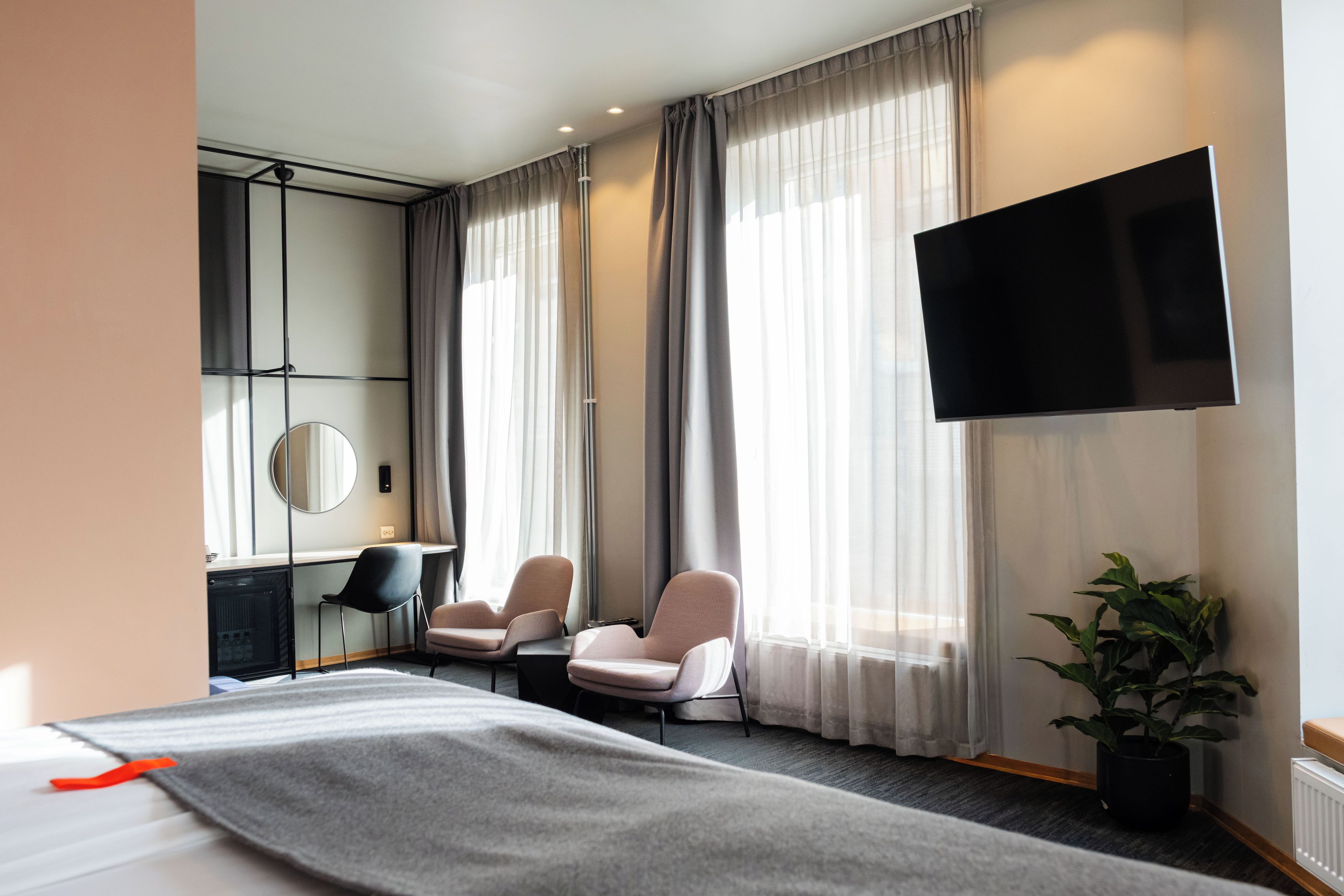 Habitación de hotel con cama, dos sillones, un escritorio, televisor de pantalla plana y un amplio ventanal con cortinas.