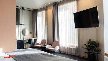Habitación de hotel con cama, dos sillones, un escritorio, televisor de pantalla plana y un amplio ventanal con cortinas.