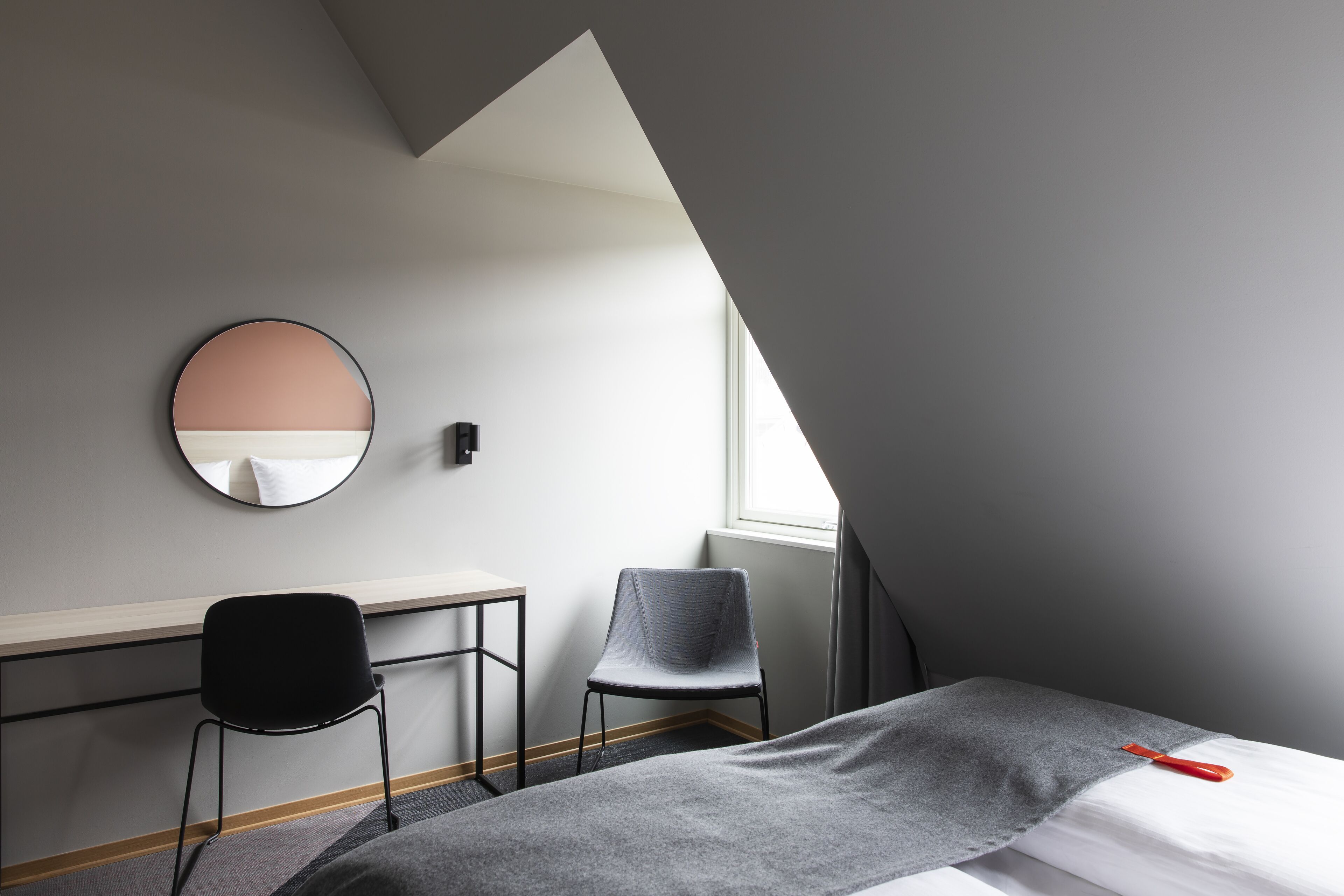 Un dormitorio moderno con una cama, dos sillas, un escritorio y un espejo redondo.