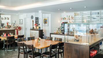 Un comedor moderno con una mesa y sillas de madera, una zona de cocina con estanterías de vidrio y diversos objetos decorativos.