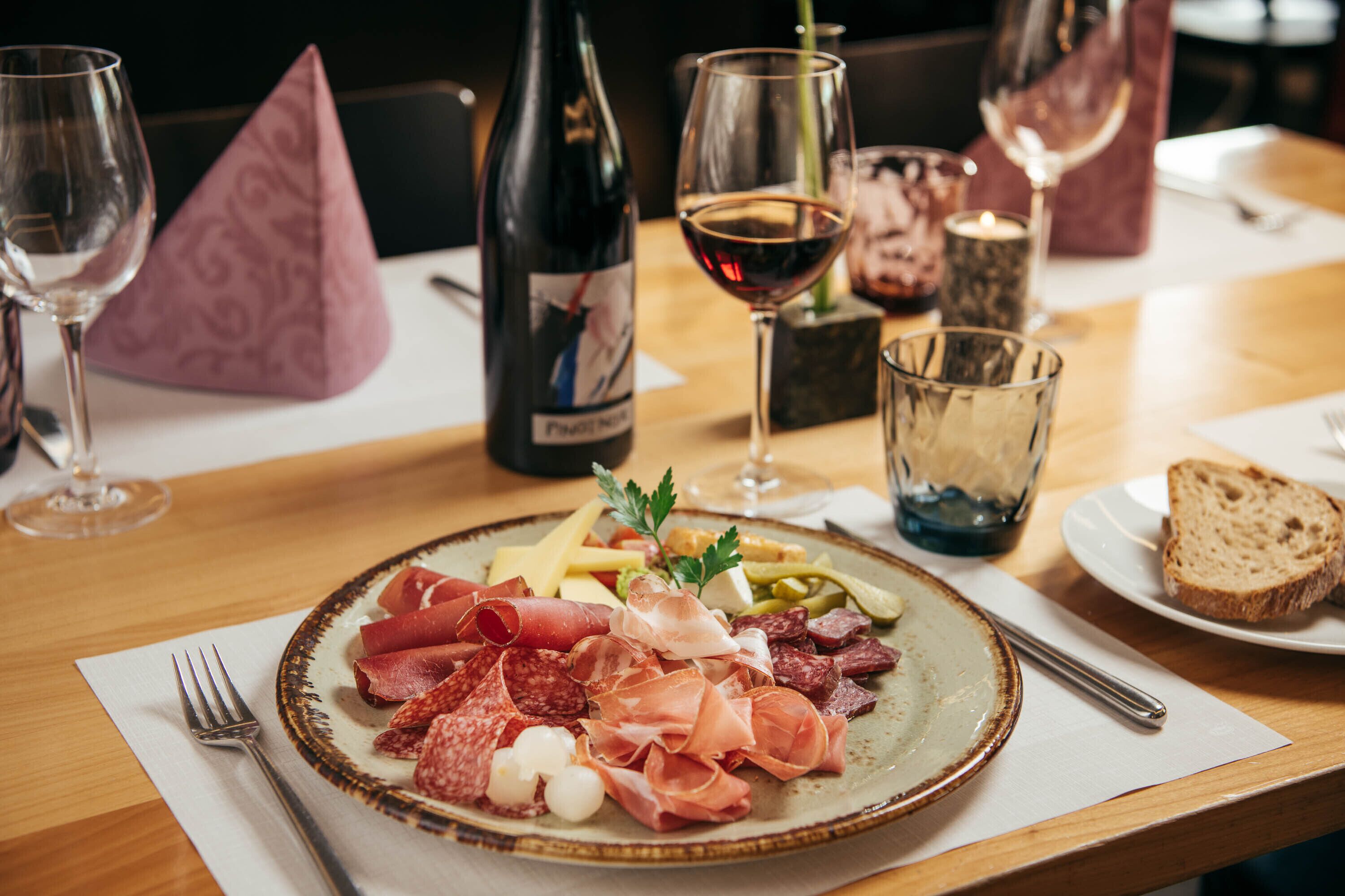 Une table avec une assiette de charcuteries variées, une bouteille de vin et des verres.