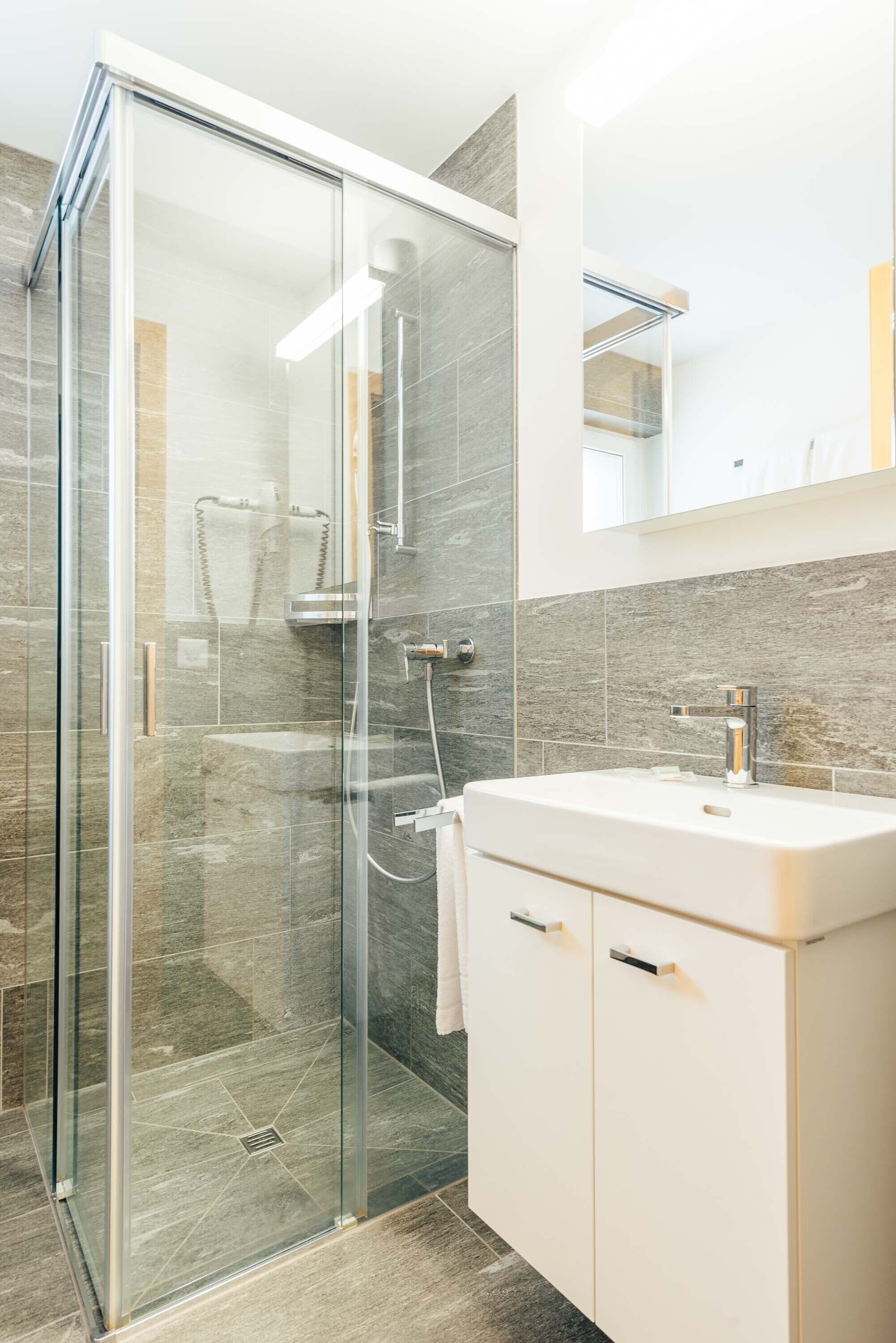 Un baño moderno con cabina de ducha de vidrio, un lavamanos blanco y un espejo grande sobre el mueble.