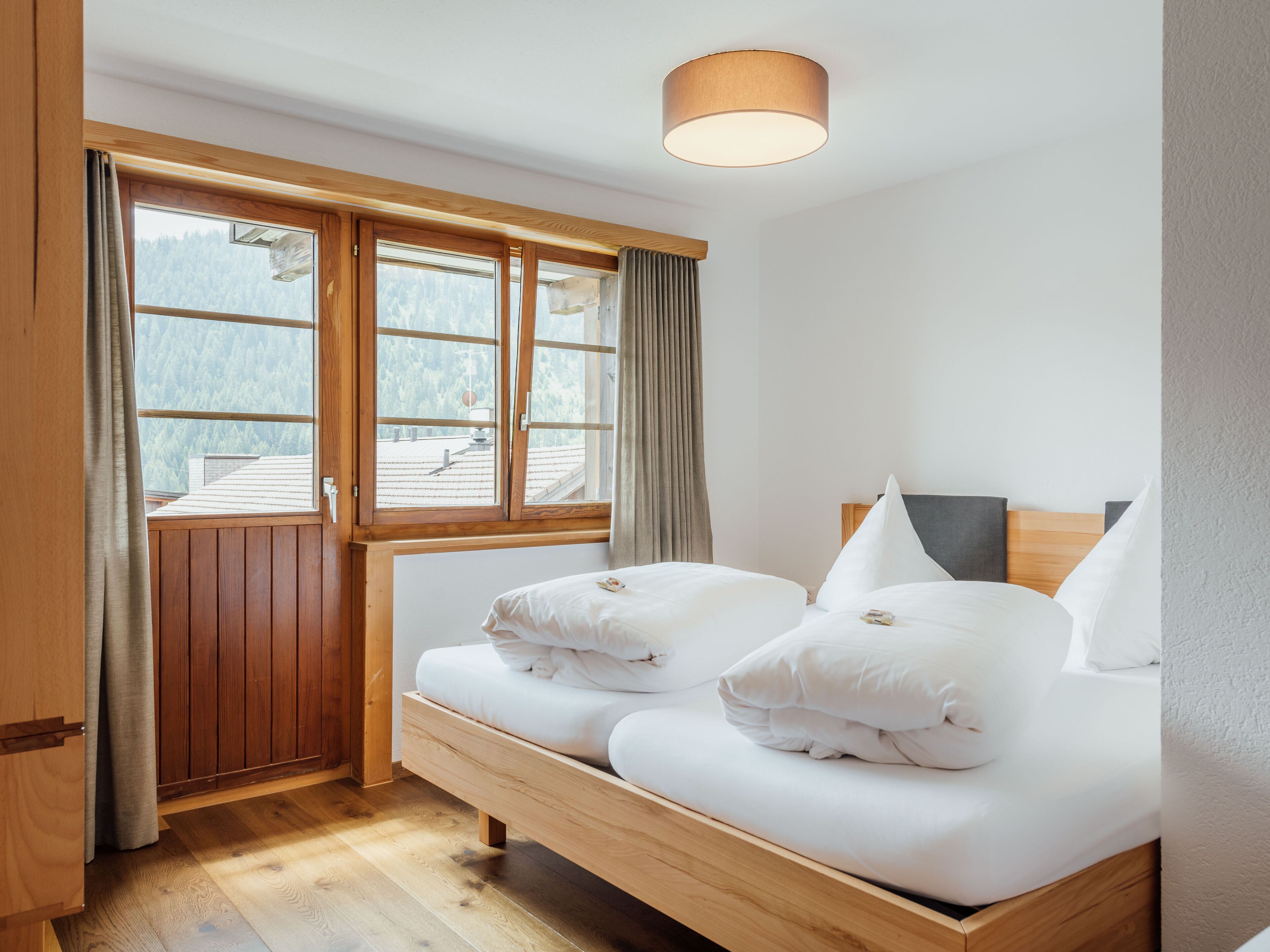 Un dormitorio con una cama de madera, una ventana con cortinas y una lámpara en el techo.