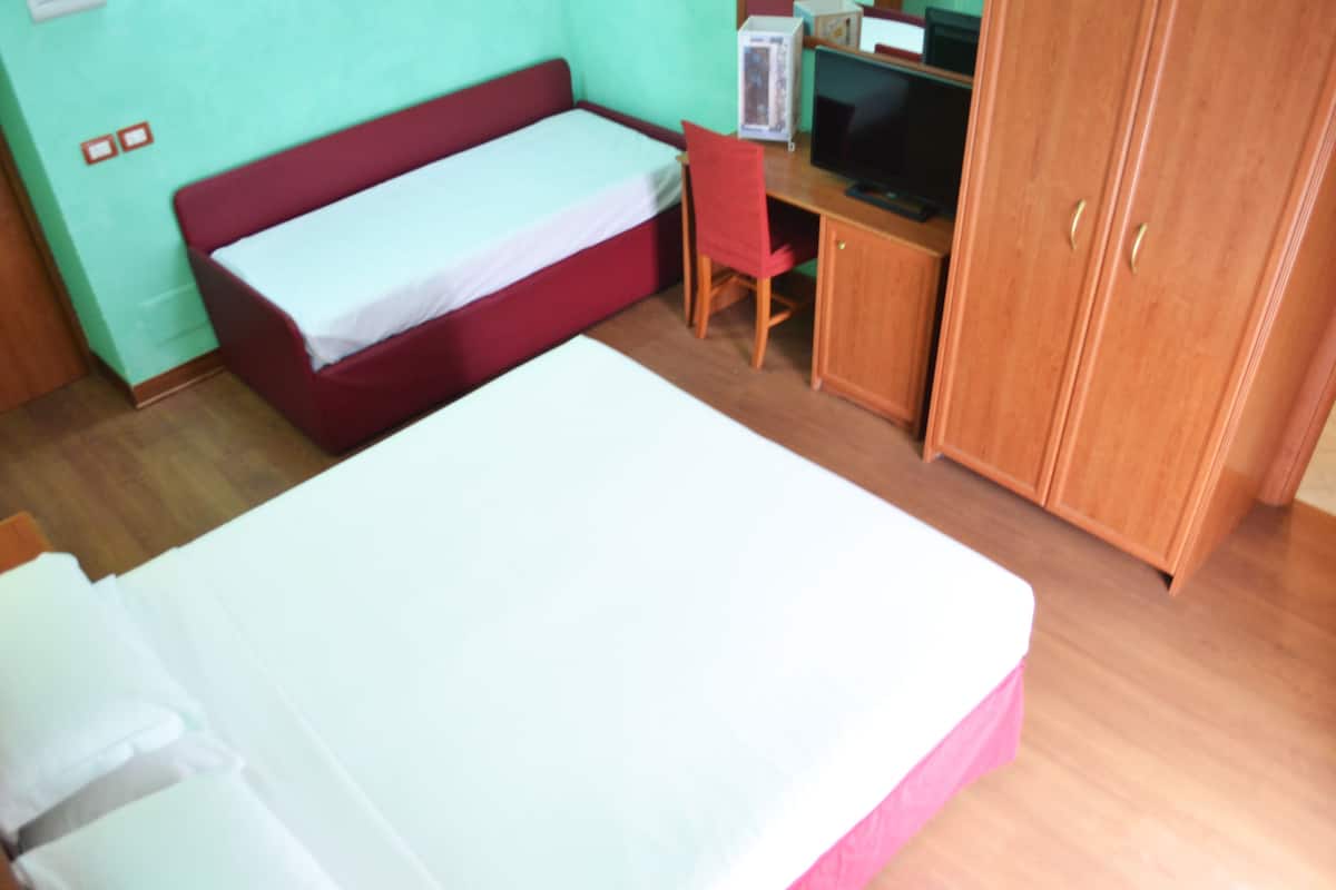 Una habitación con cama, un escritorio con computadora, televisor y armario.