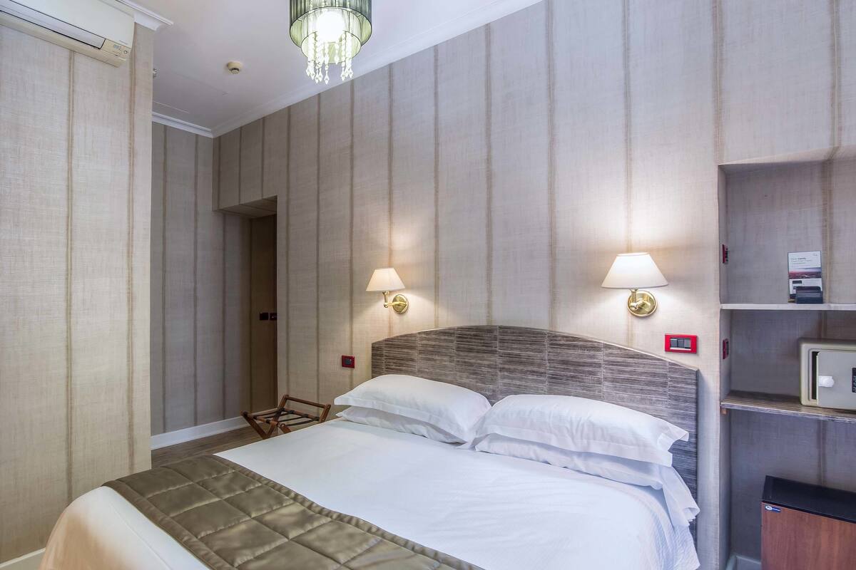 Una habitación de hotel con una cama grande, dos lámparas de pared, un cabecero de madera y un mueble empotrado para televisión.