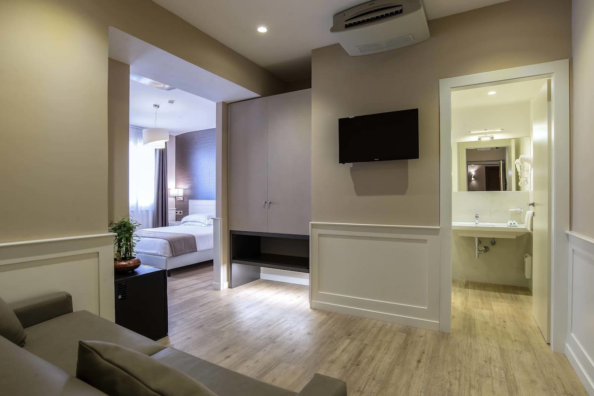 Una habitación de hotel moderna con cama, televisor, un pequeño escritorio y baño con lavamanos y espejo.