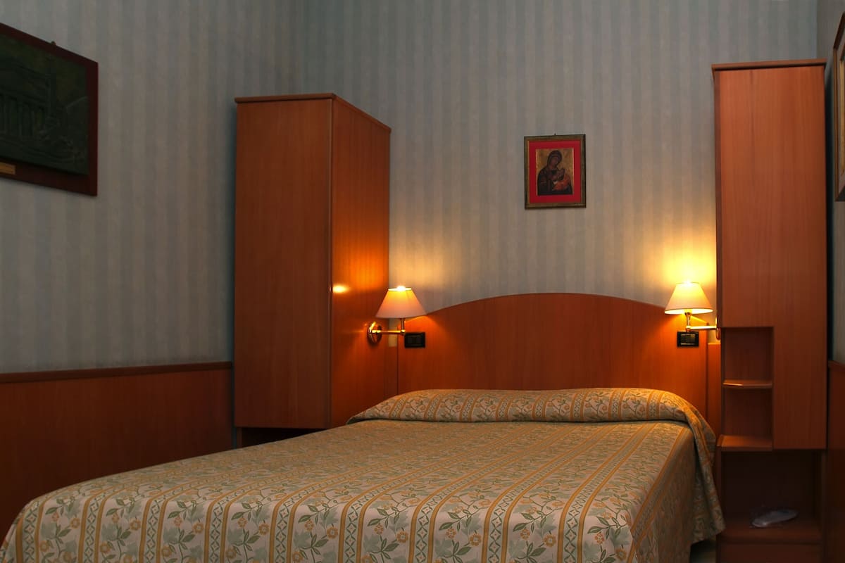 Habitación de hotel con una cama, dos lámparas de pared, un armario y un cuadro en la pared.
