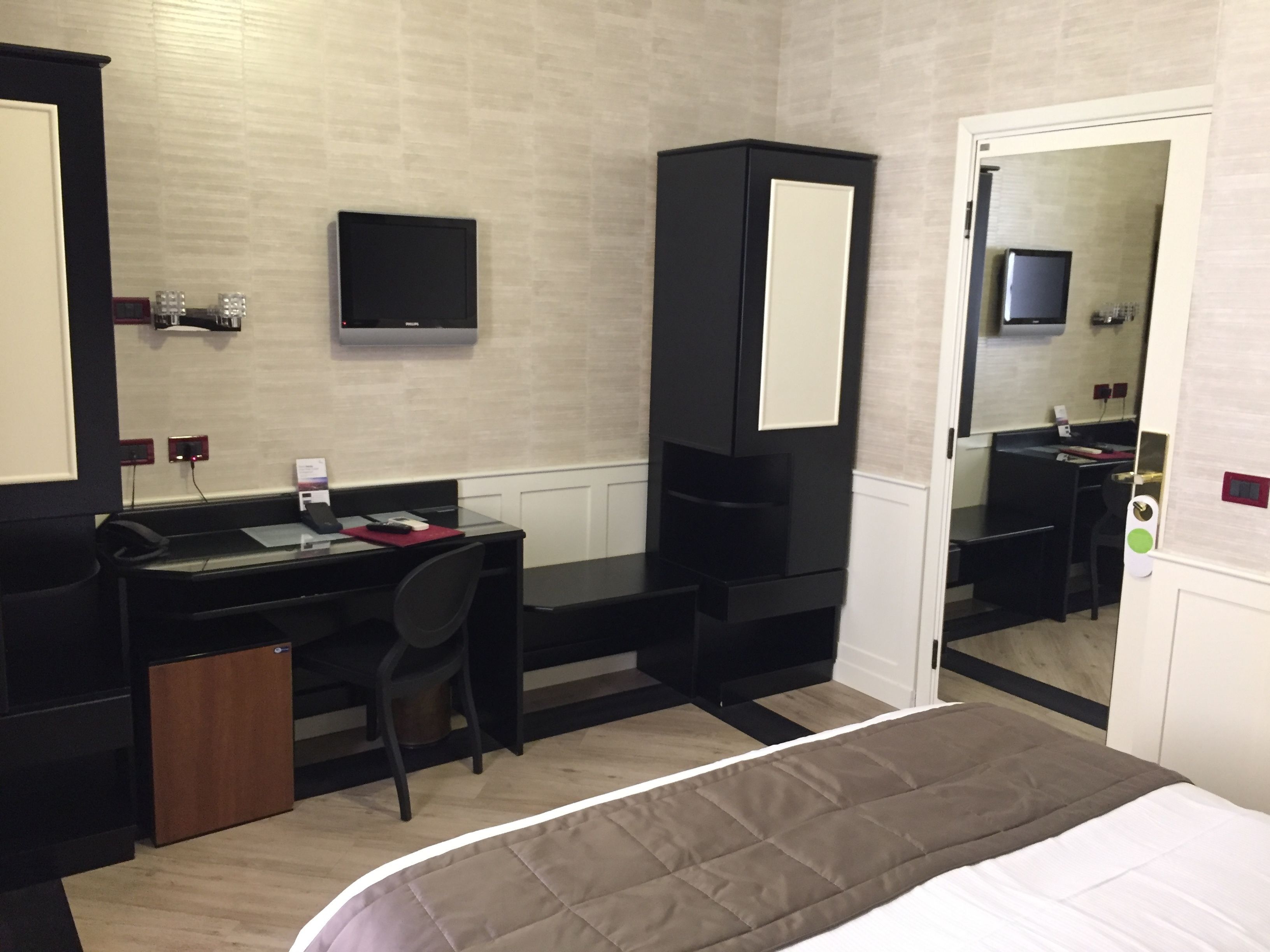 A hotel room with a bed, a desk, a chair, a television, and a wardrobe.