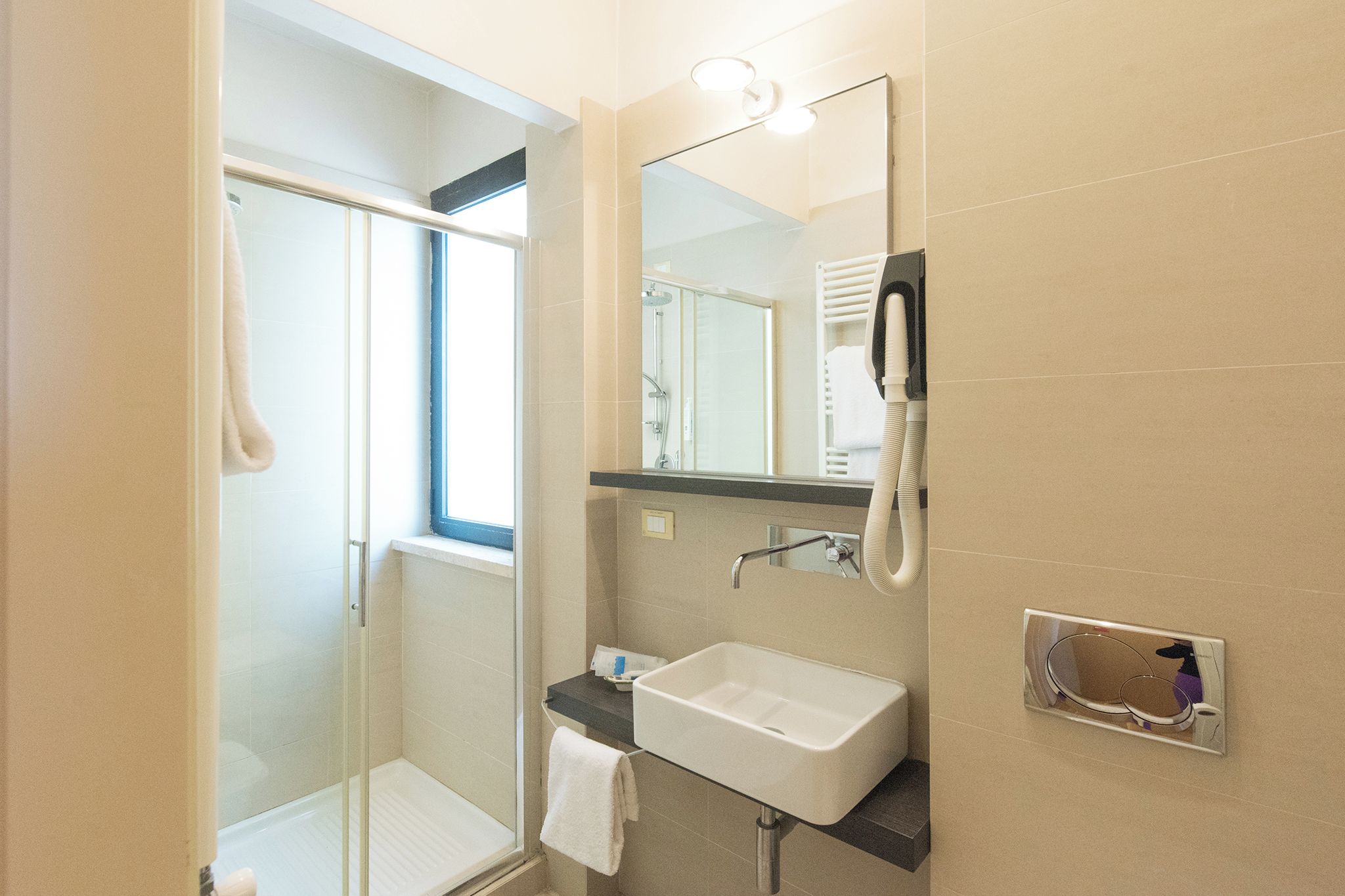 Un baño moderno con cabina de ducha de vidrio, lavabo blanco y un espejo grande.
