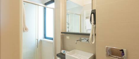 Un baño moderno con cabina de ducha de vidrio, lavabo blanco y un espejo grande.
