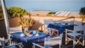 Terraza con dos mesas dispuestas para comer, con vista a una playa.